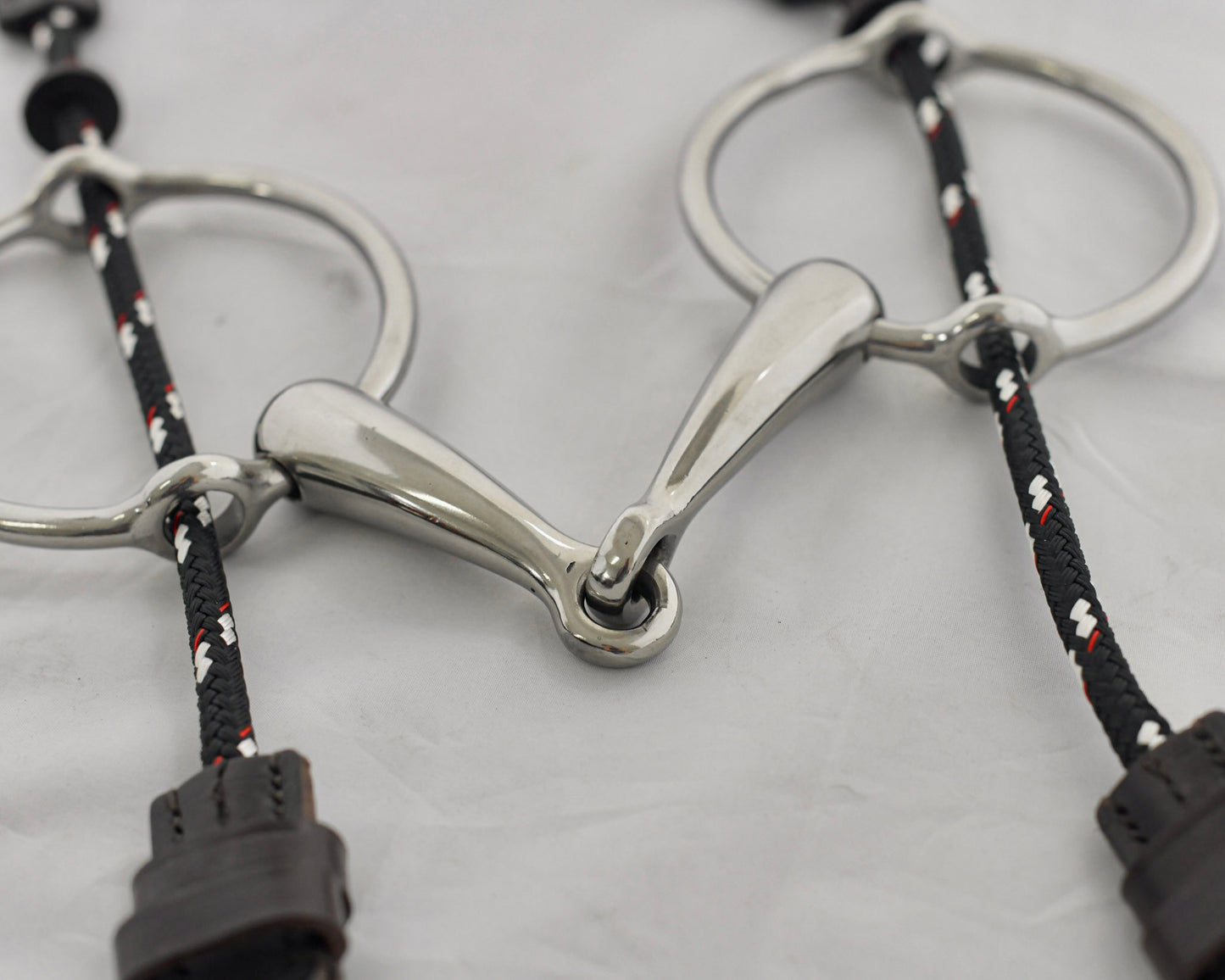 Close up of big ring gag horse bit on a white surface.
