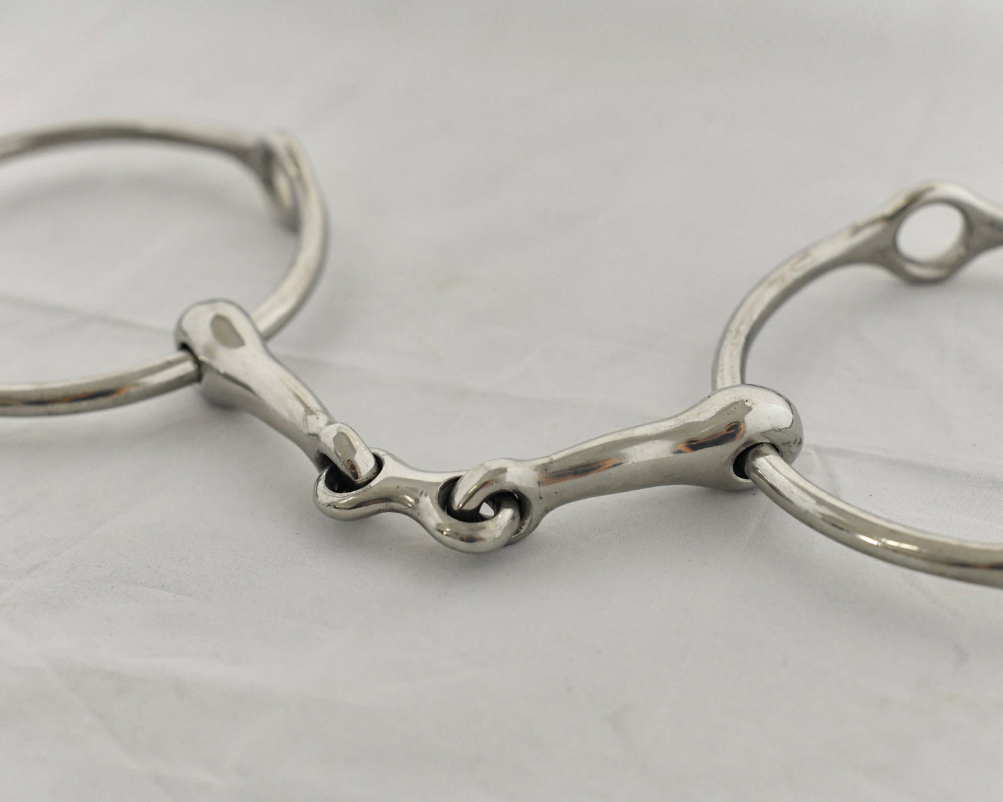 Close up of center link gag horse bit on a white surface.