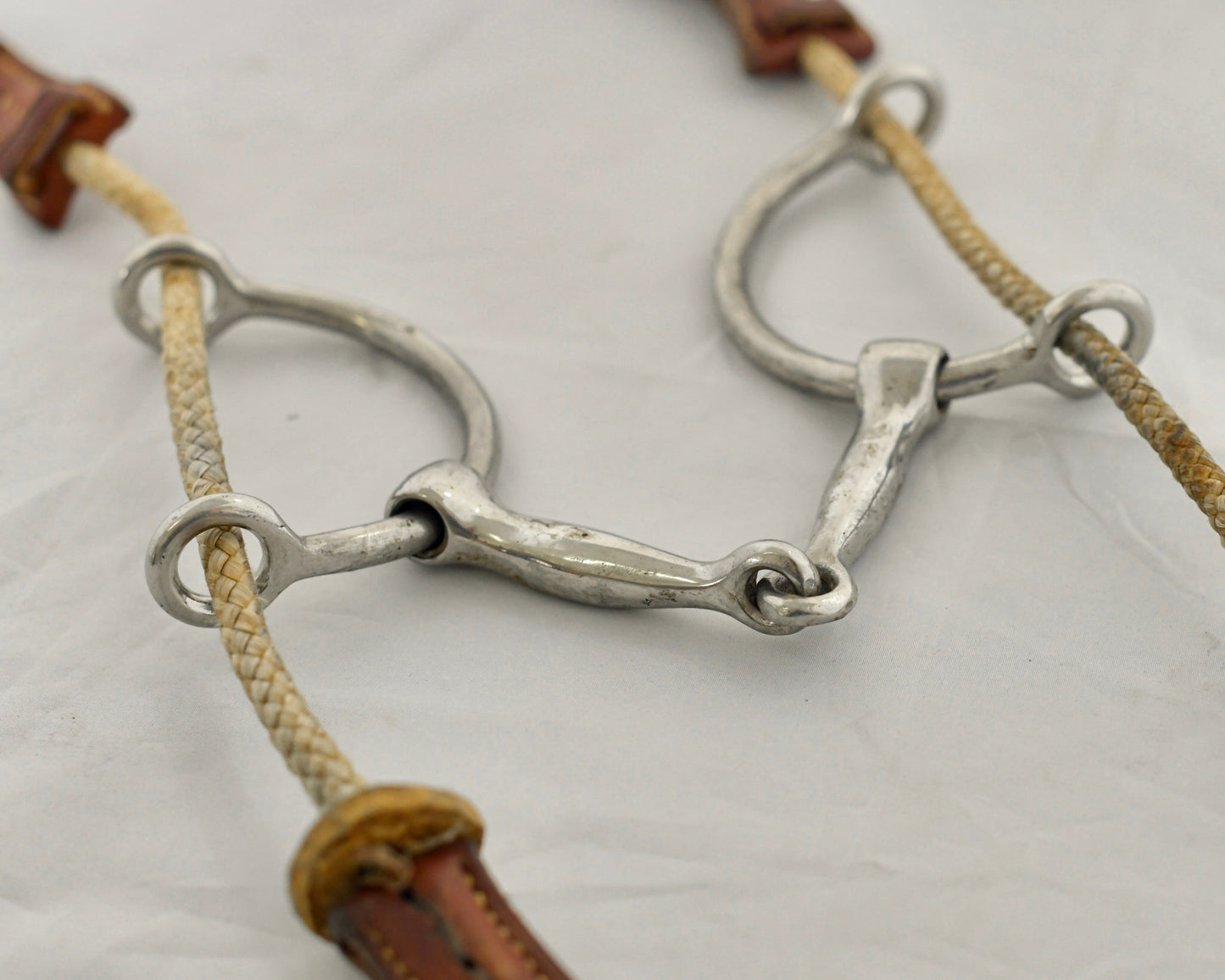 Close up of large balding gag horse bit on a white surface.