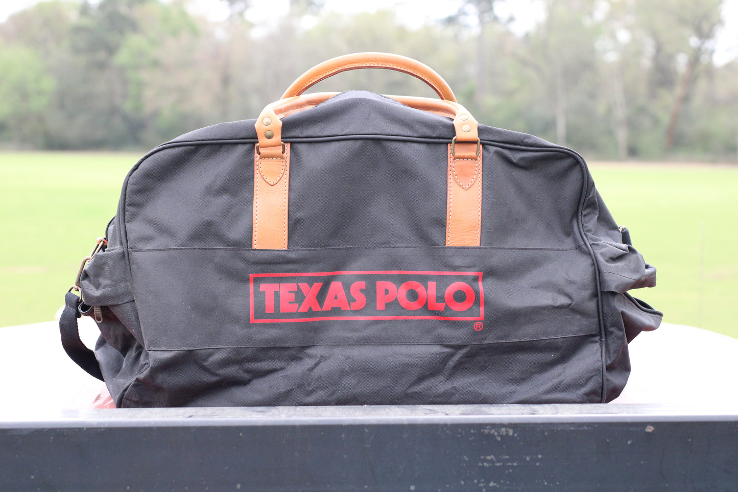 Front view of black travel bag with red Texas Polo logo and tan leather handles.