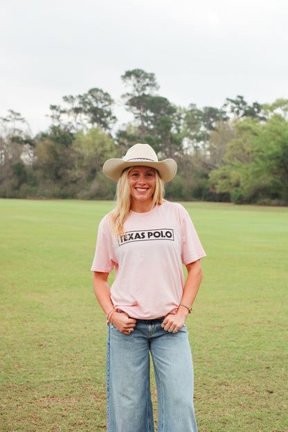 Woman wearing a pink t-shirt with black Texas Polo logo and a tan cowboy hat.