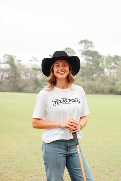 Woman wearing a white t-shirt with black Texas Polo logo and black cowboy hat, holding a polo mallet.