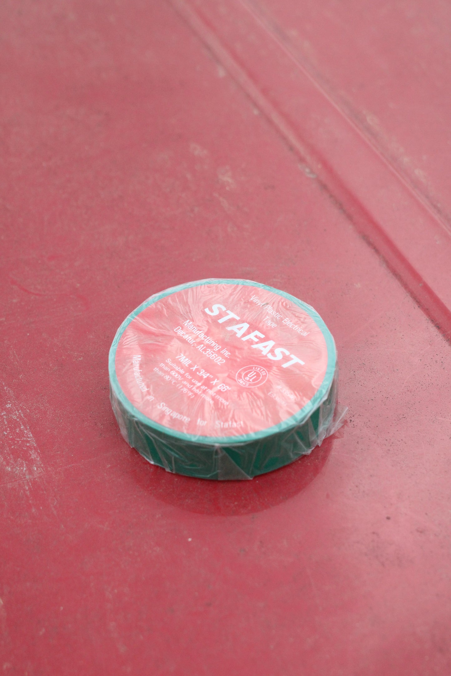 Roll of green electrical tape in clear wrap sitting on a red surface.