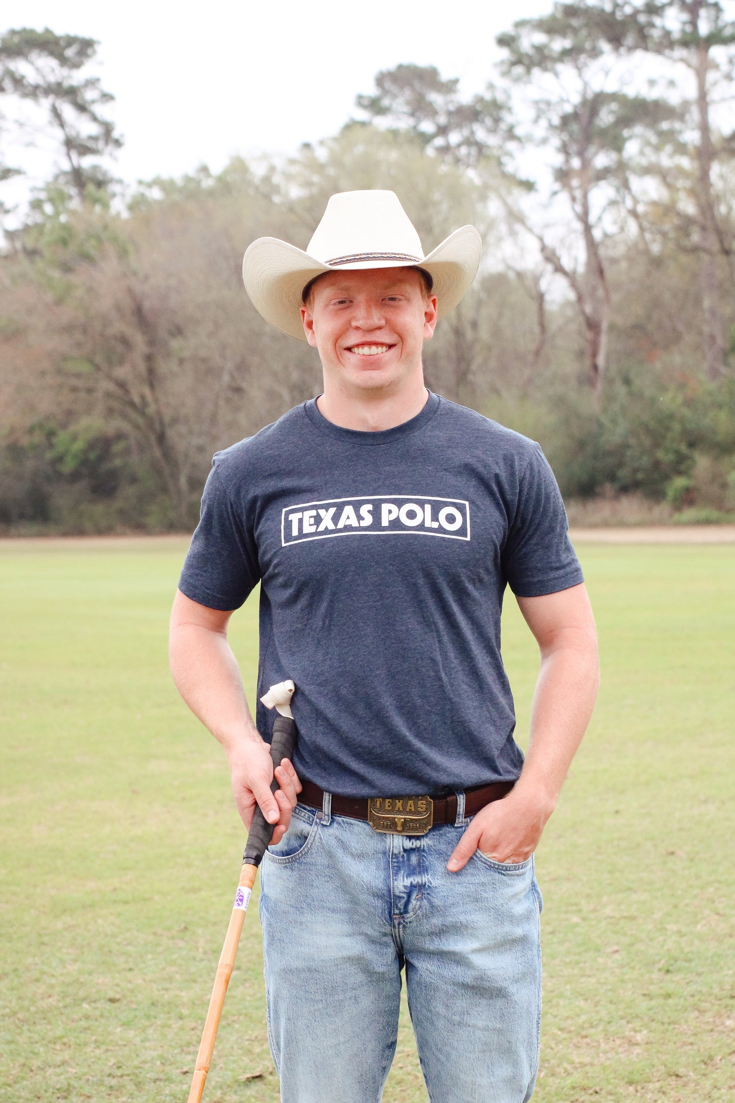 Man wearing a grey t-shirt with white Texas Polo logo and tan cowboy hat, holding a polo mallet.