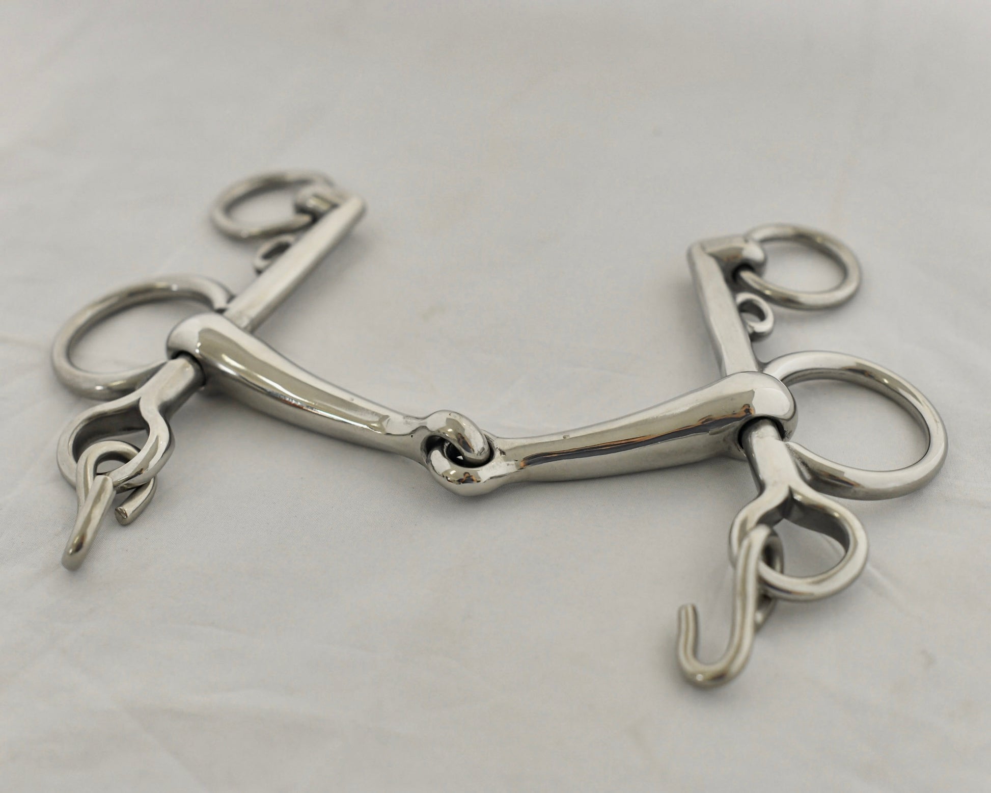 Close up of jointed pelham horse bit on a white surface.