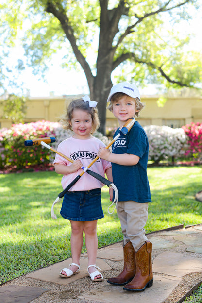 Two children wearing Texas Polo t-shirts in pink and navy and a white Texas Polo hat. They are each holding a foot mallet crossed in front of them.