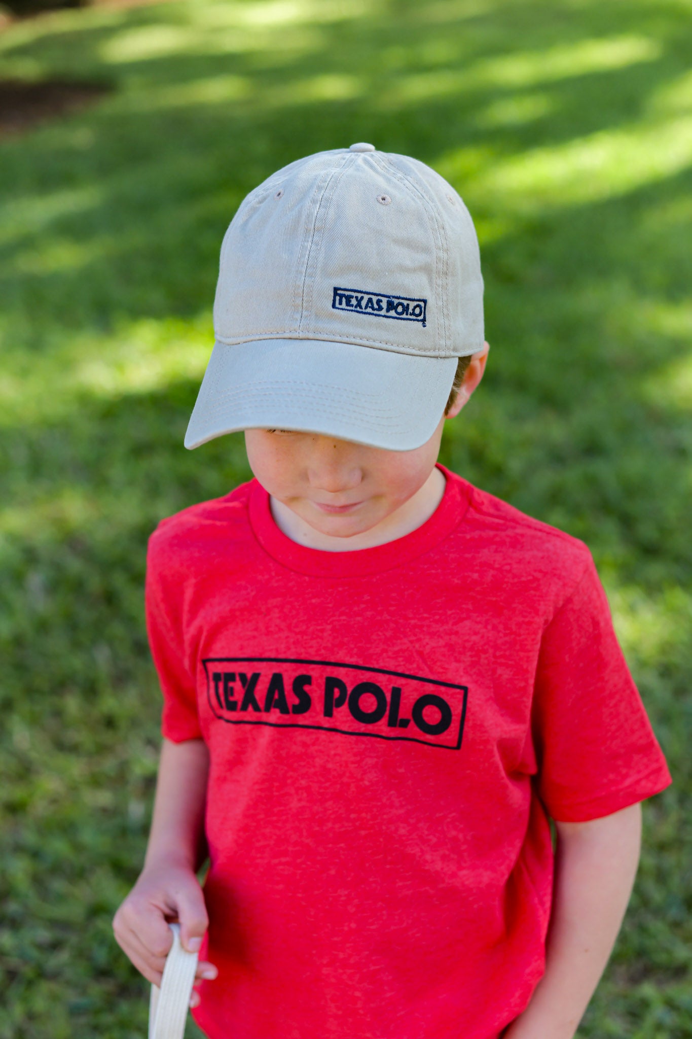 Child wearing a tan Texas Polo hat and red t-shirt with black Texas Polo logo.