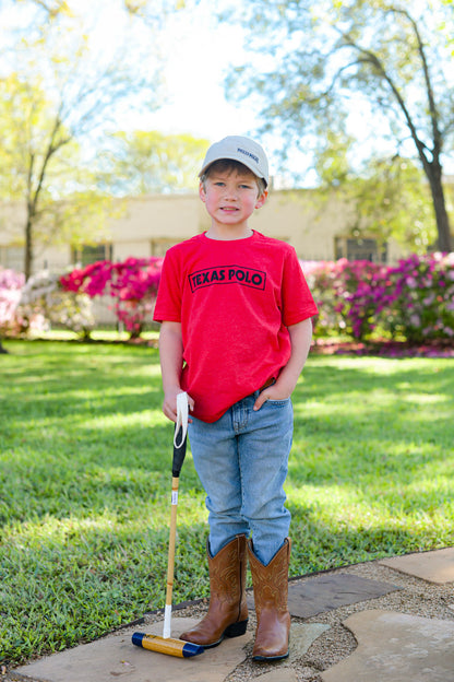 Child wearing a red t-shirt with black Texas Polo logo and tan Texas Polo branded hat, holding a mallet.