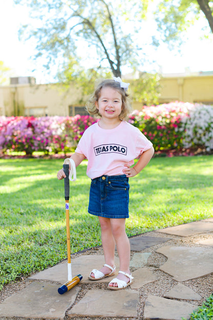 Child holding a polo foot mallet and wearing a pink t-shirt with a black Texas Polo logo.