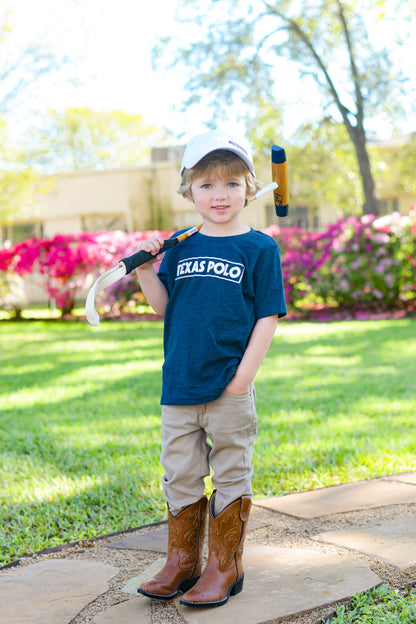Child wearing a navy t-shirt with white Texas Polo logo and white Texas Polo branded cap, with a mallet over his shoulder.