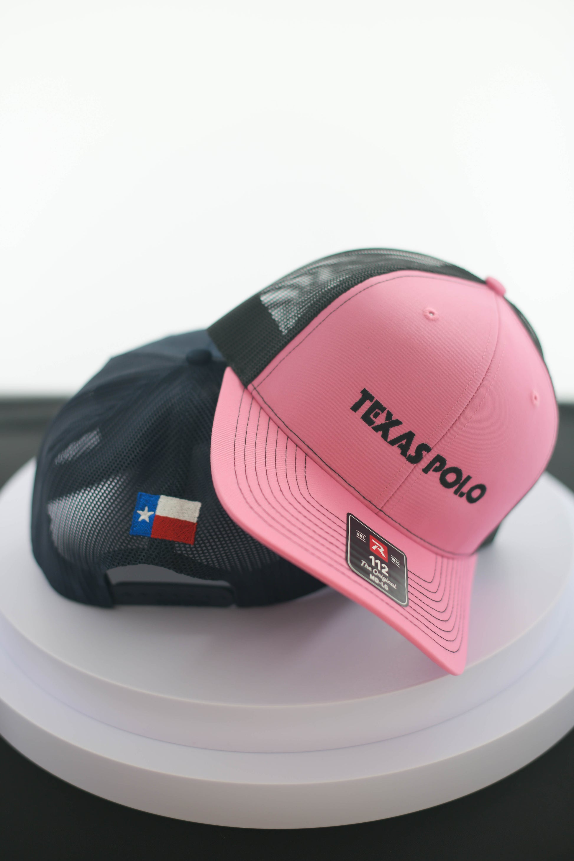 Pink Texas Polo branded cap on top of the back of a navy cap with the Texas flag showing.