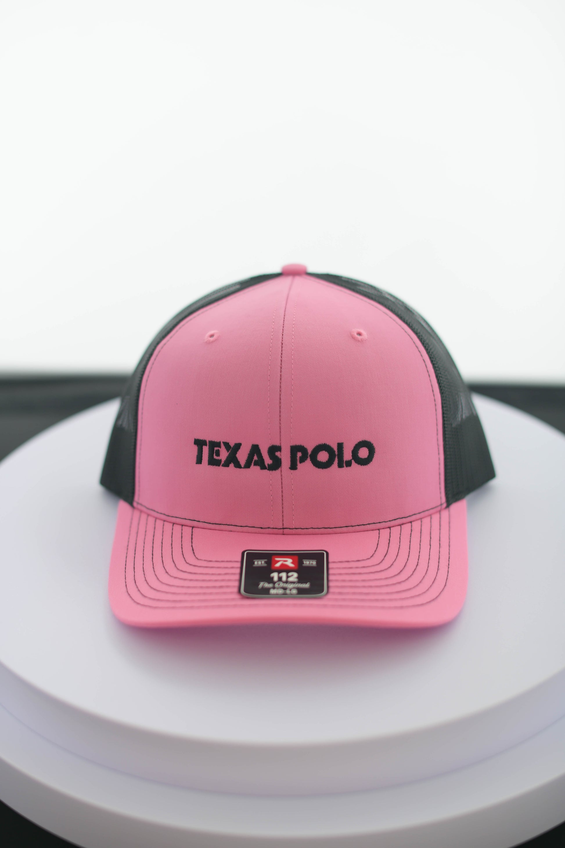 Pink and black Texas Polo cap on a white surface.