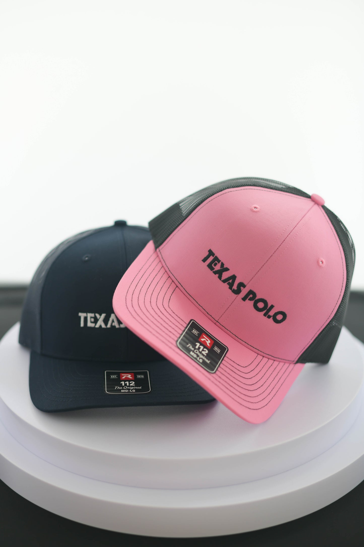 Pink Texas Polo cap leaning on a navy Texas Polo cap.