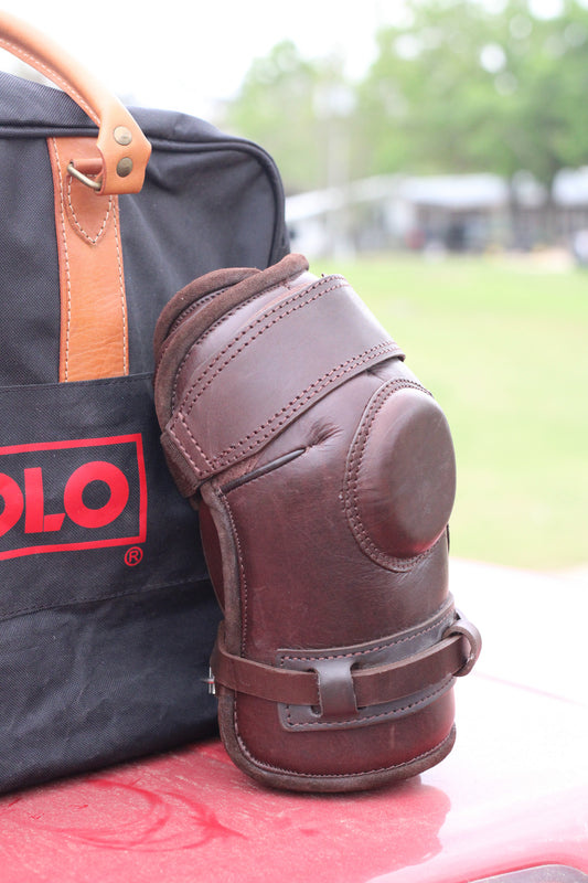 Side view of brown leather knee guard leaning against a black travel bag.