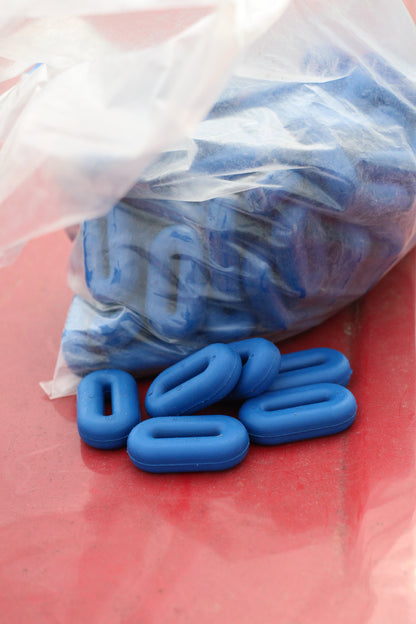 Bag of blue rubber martingale stoppers with a few sitting outside of the bag on a red surface.