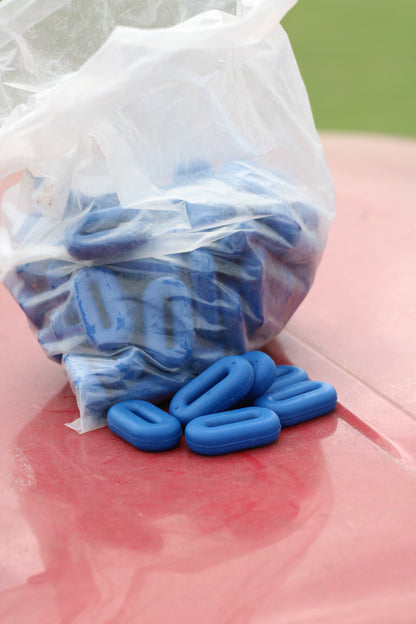 Bag of blue rubber martingale stoppers with a few sitting outside of the bag on a red surface.