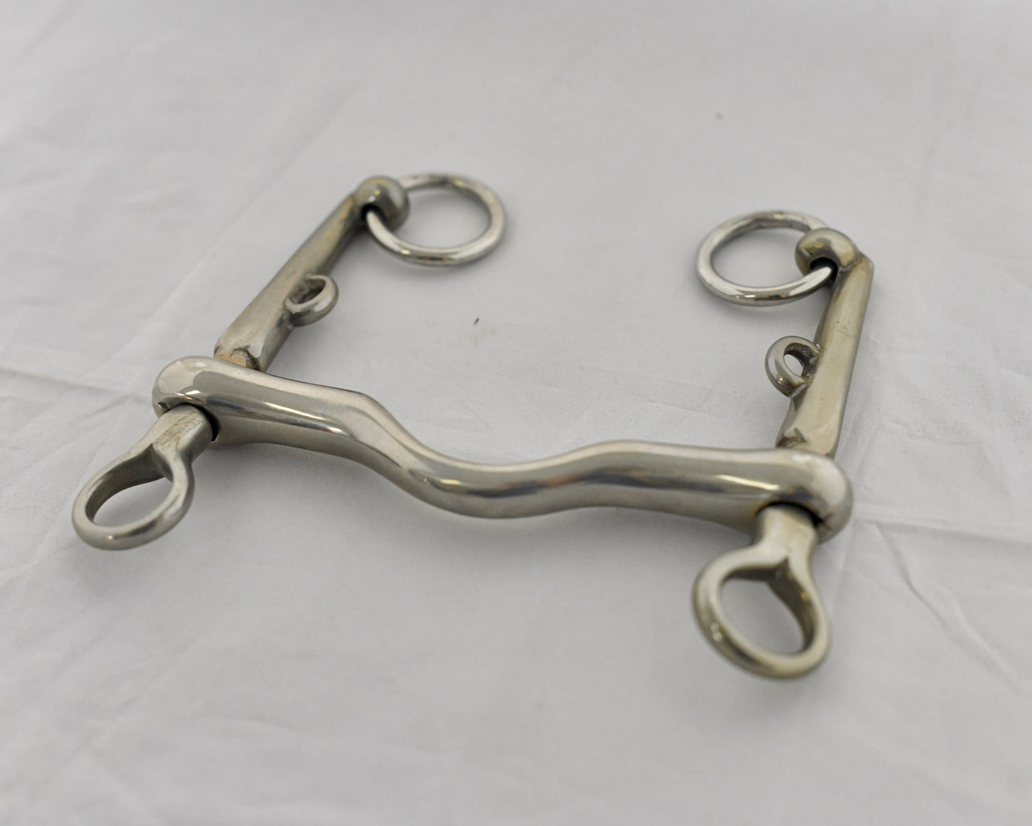 Close up of pelham horse bit on a white surface.