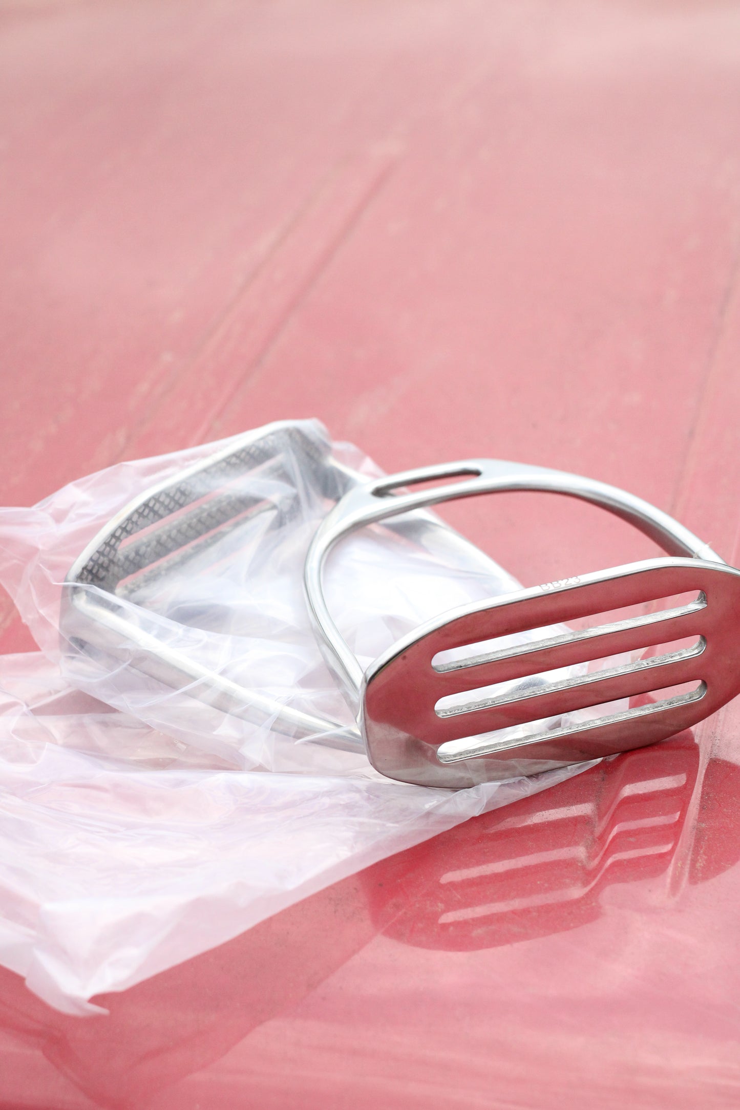 Pair of silver stirrup irons sitting on a red surface.