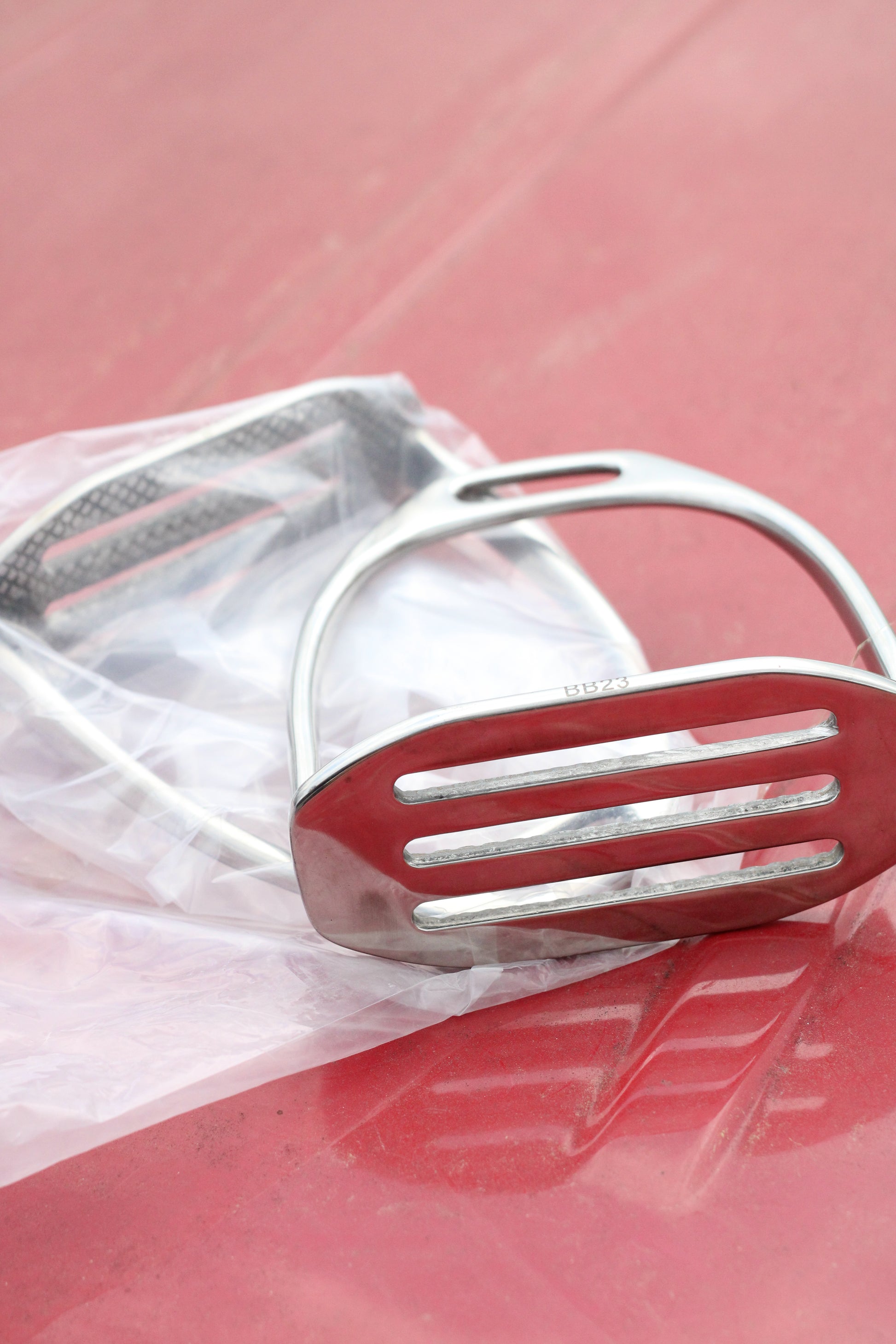Pair of silver stirrup irons sitting on a red surface.