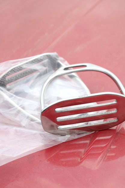 Pair of silver stirrup irons sitting on a red surface.