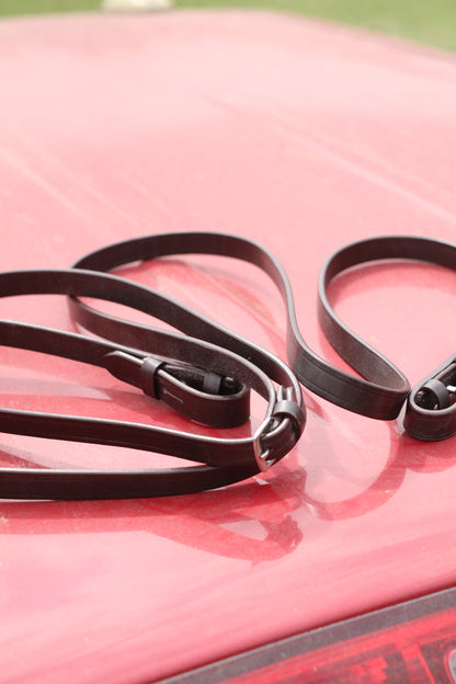 Brown leather straight reins sitting on a red surface.