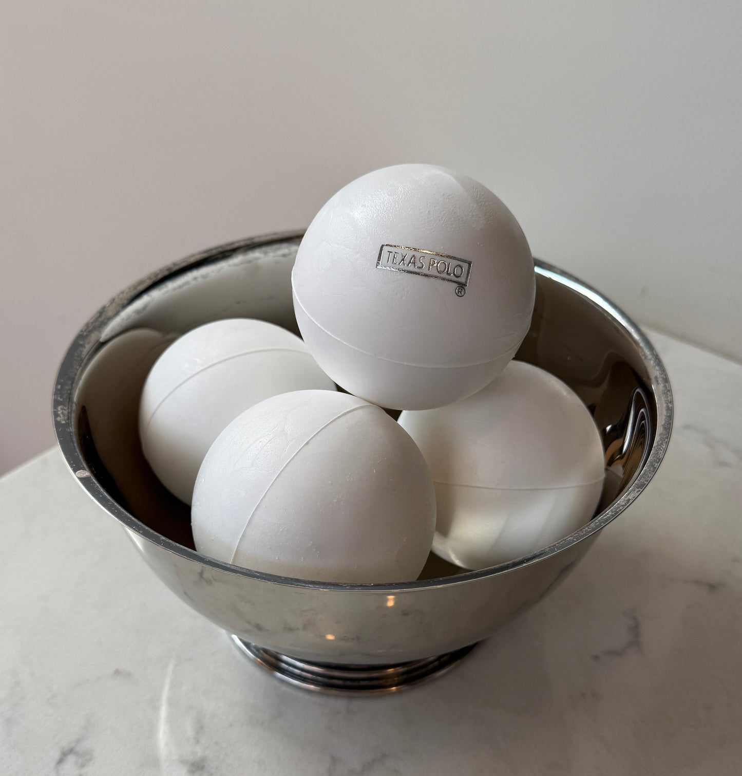White Texas Polo branded polo balls sitting in a metal bowl.