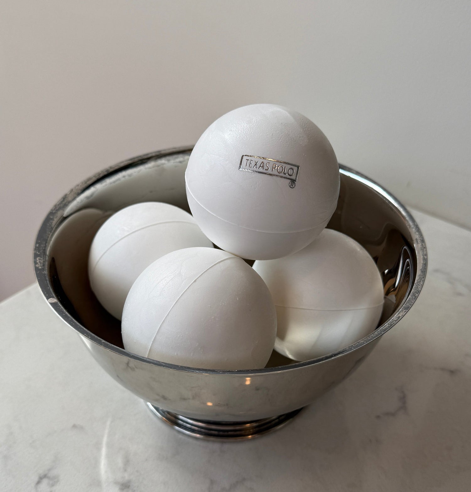 White Texas Polo branded polo balls sitting in a metal bowl.