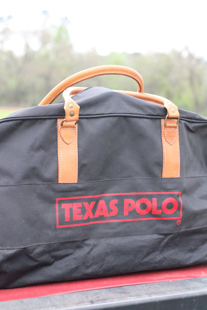 Side view of black travel bag with red Texas Polo logo and tan leather handles.