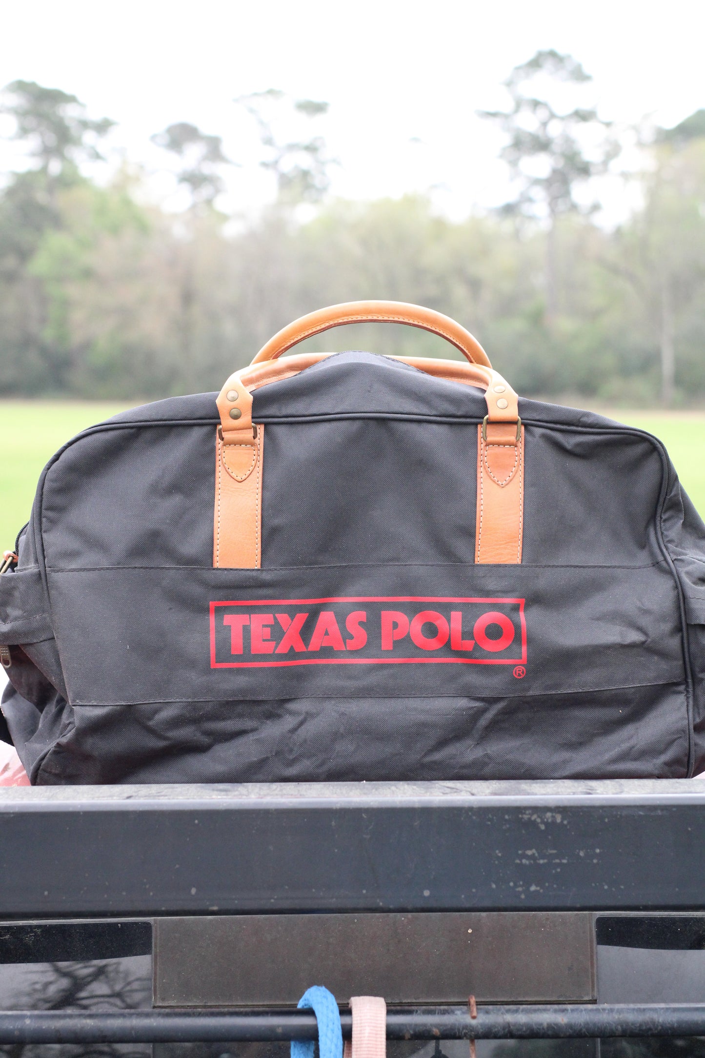 Front view of black travel bag with red Texas Polo logo and tan leather handles.