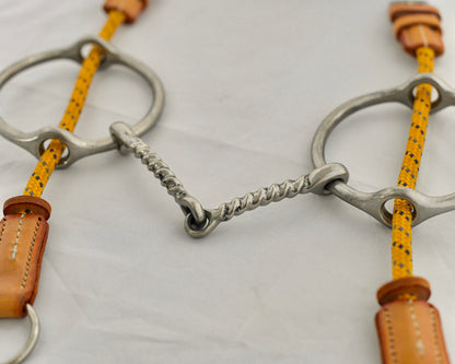 Close up of twisted big ring gag horse bit on a white surface.