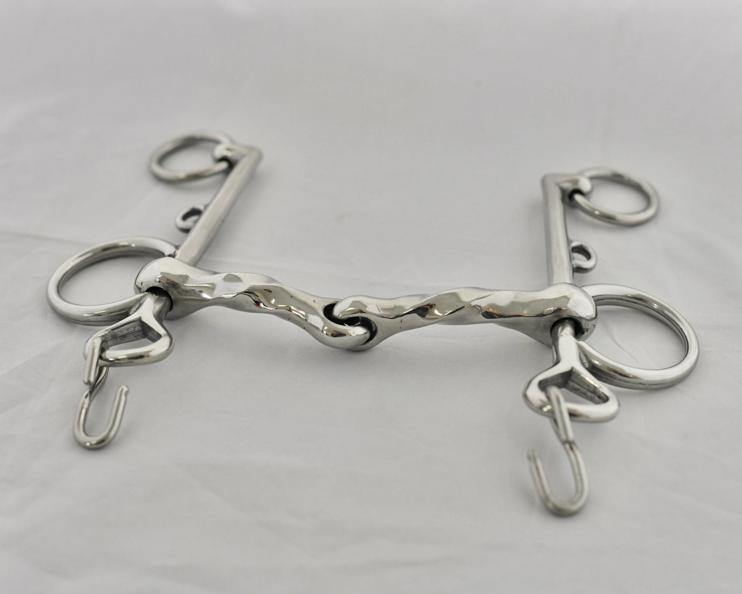 Close up of twisted jointed pelham horse bit on a white surface.